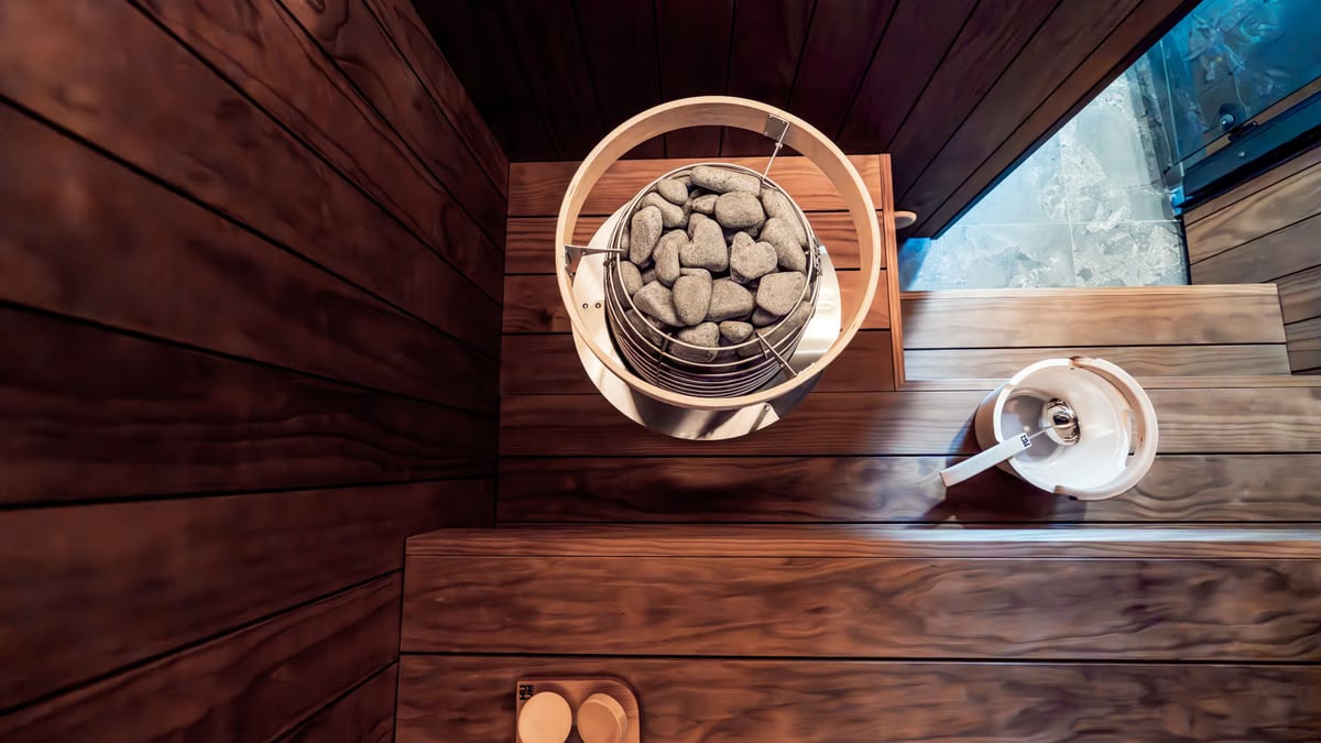 Top view of a stylish Nordic sauna featuring an electric heater, wooden benches, and warm lighting for a cozy indoor relaxation space.